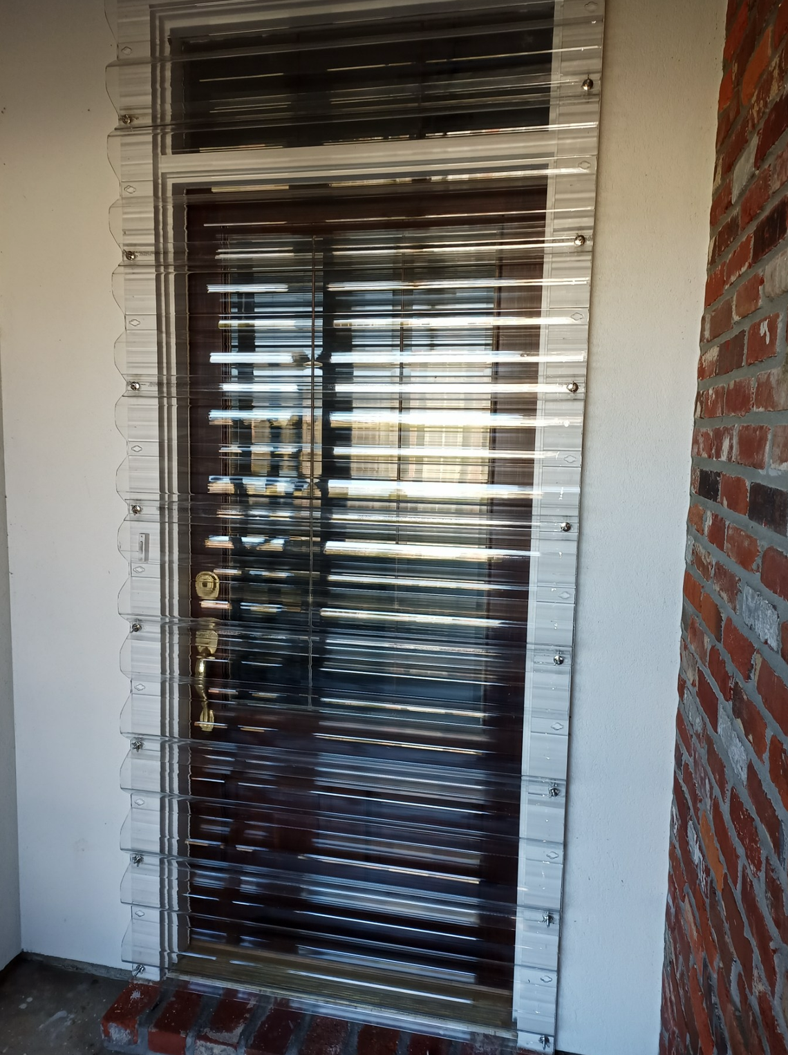 A door with a clear plastic screen on it and a brick wall behind it.