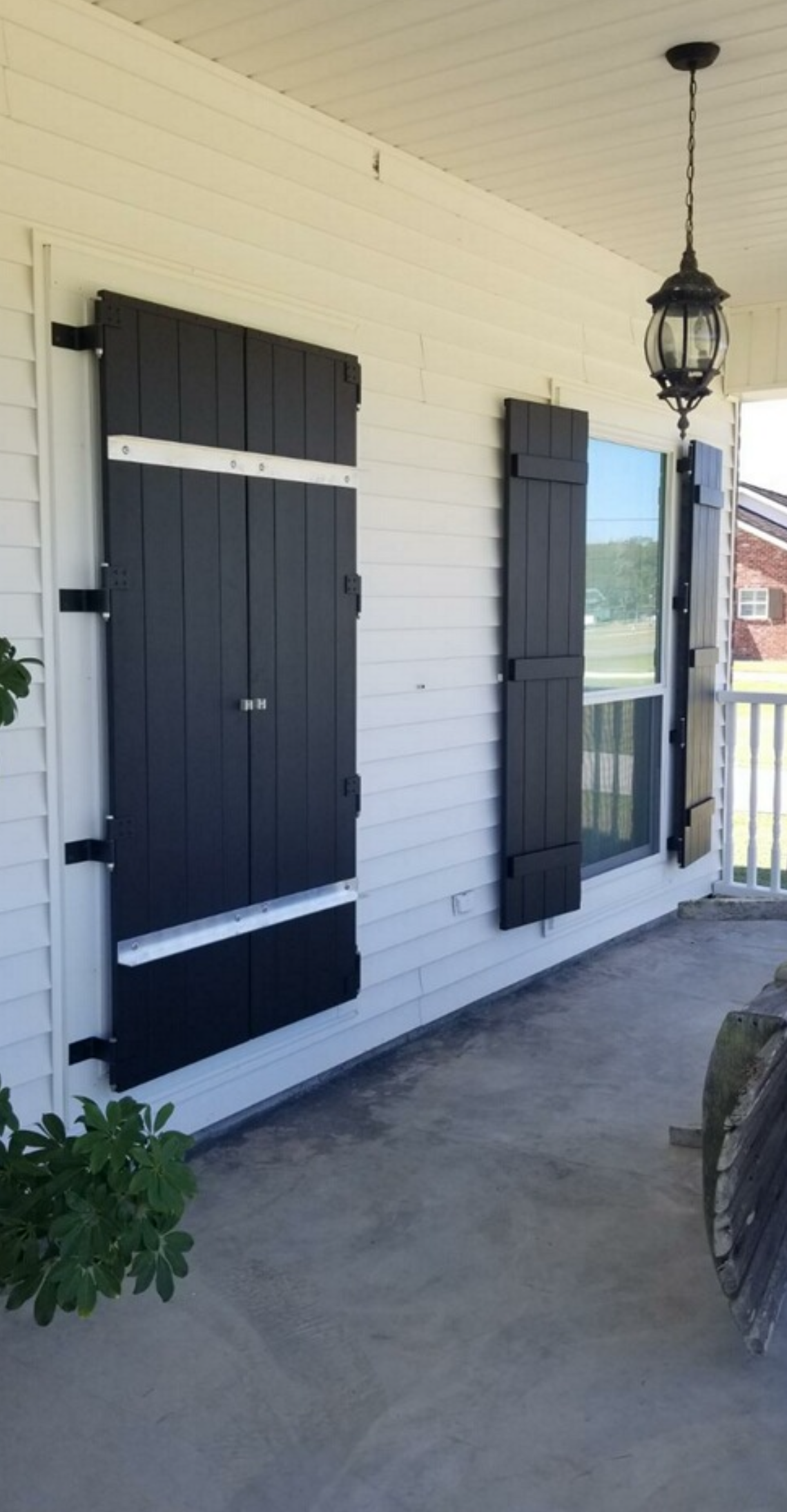 A porch with black shutters on the windows of a house.
