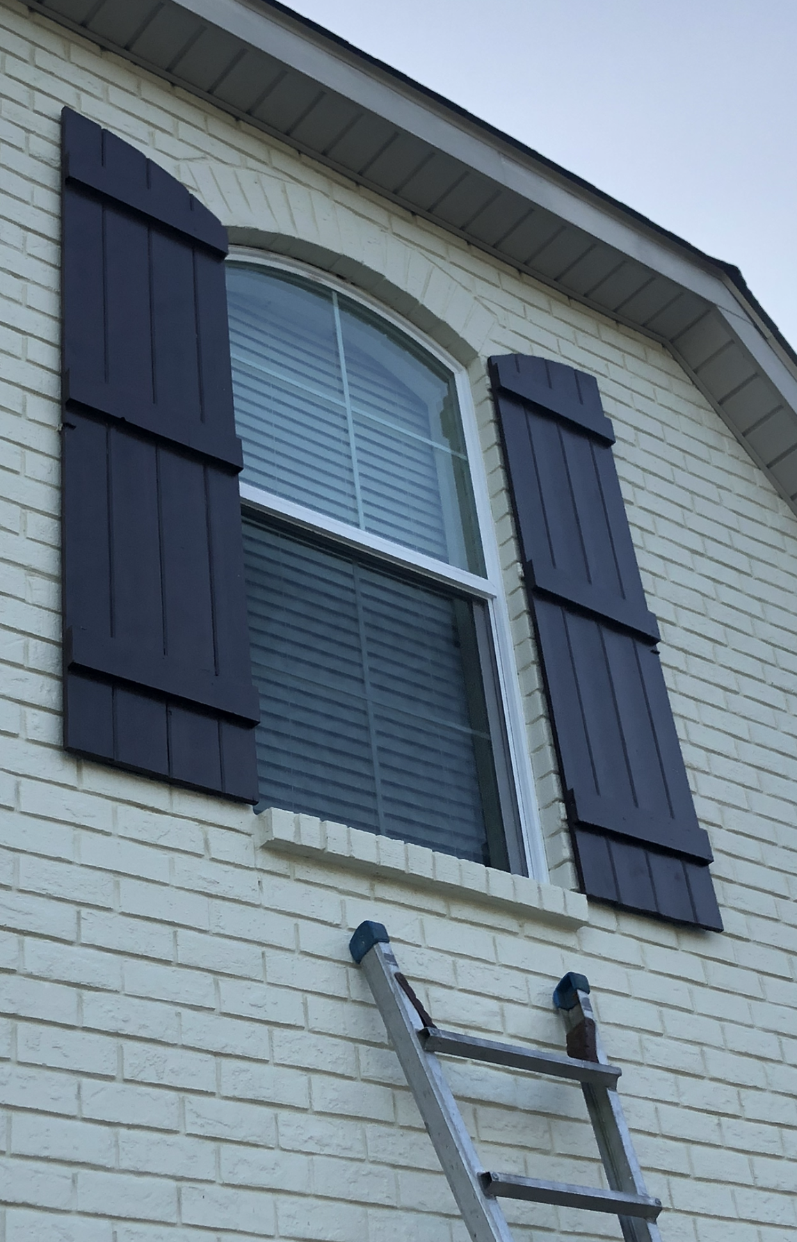 A white brick house with black shutters and a ladder.
