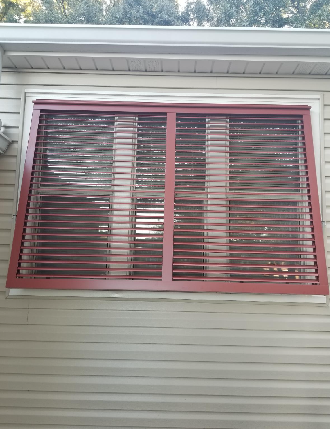 A window with red blinds on it is on the side of a house.