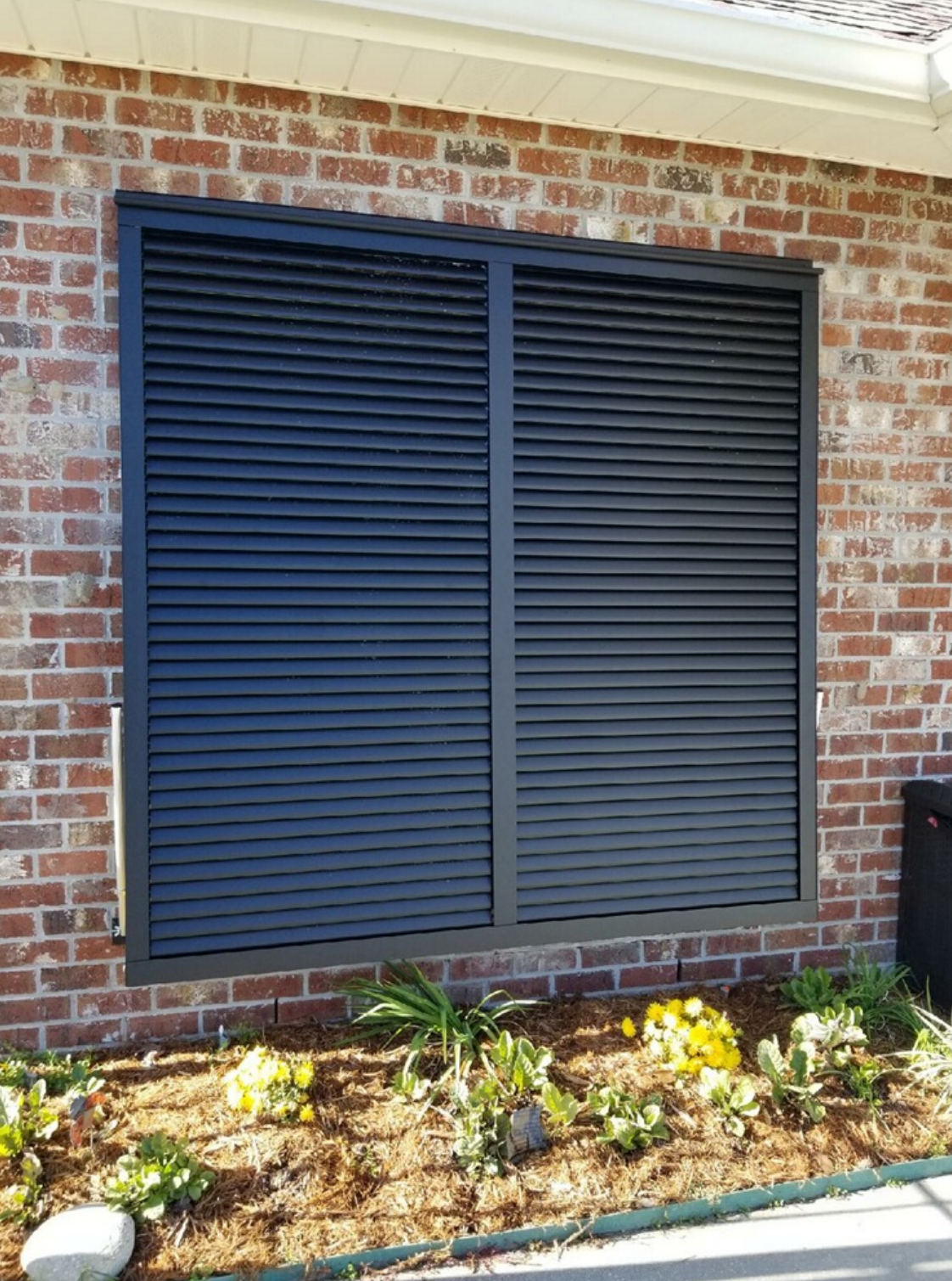 A brick building with a window with black shutters on it.