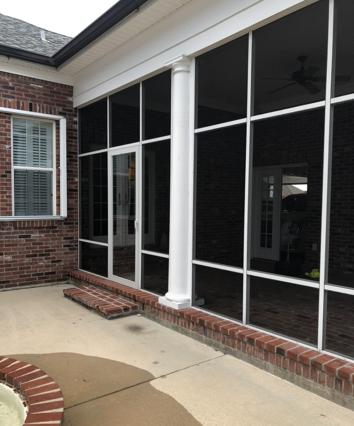 A screened in porch with a brick wall and black windows.