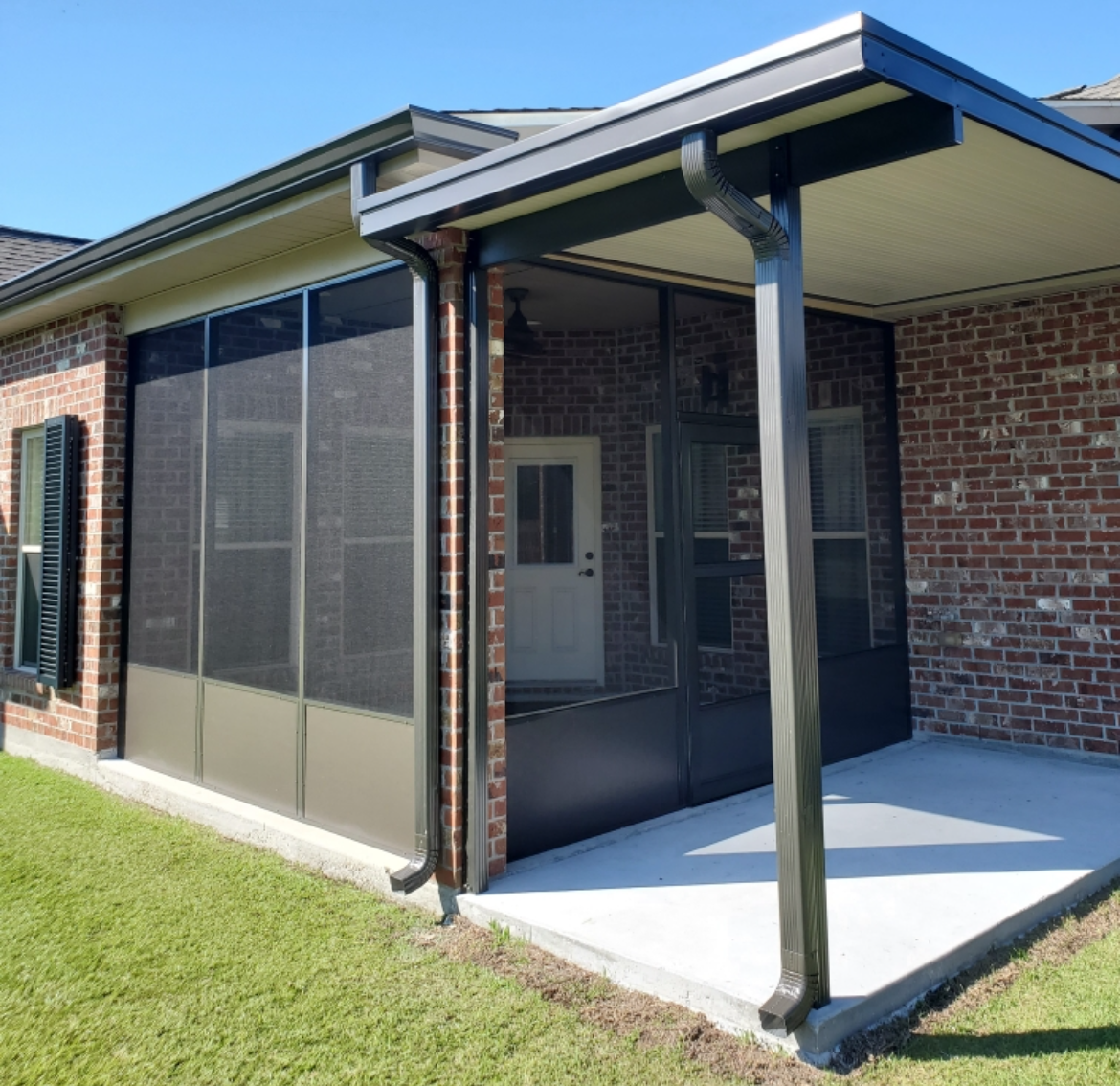 A screened in porch with a brick house in the background.