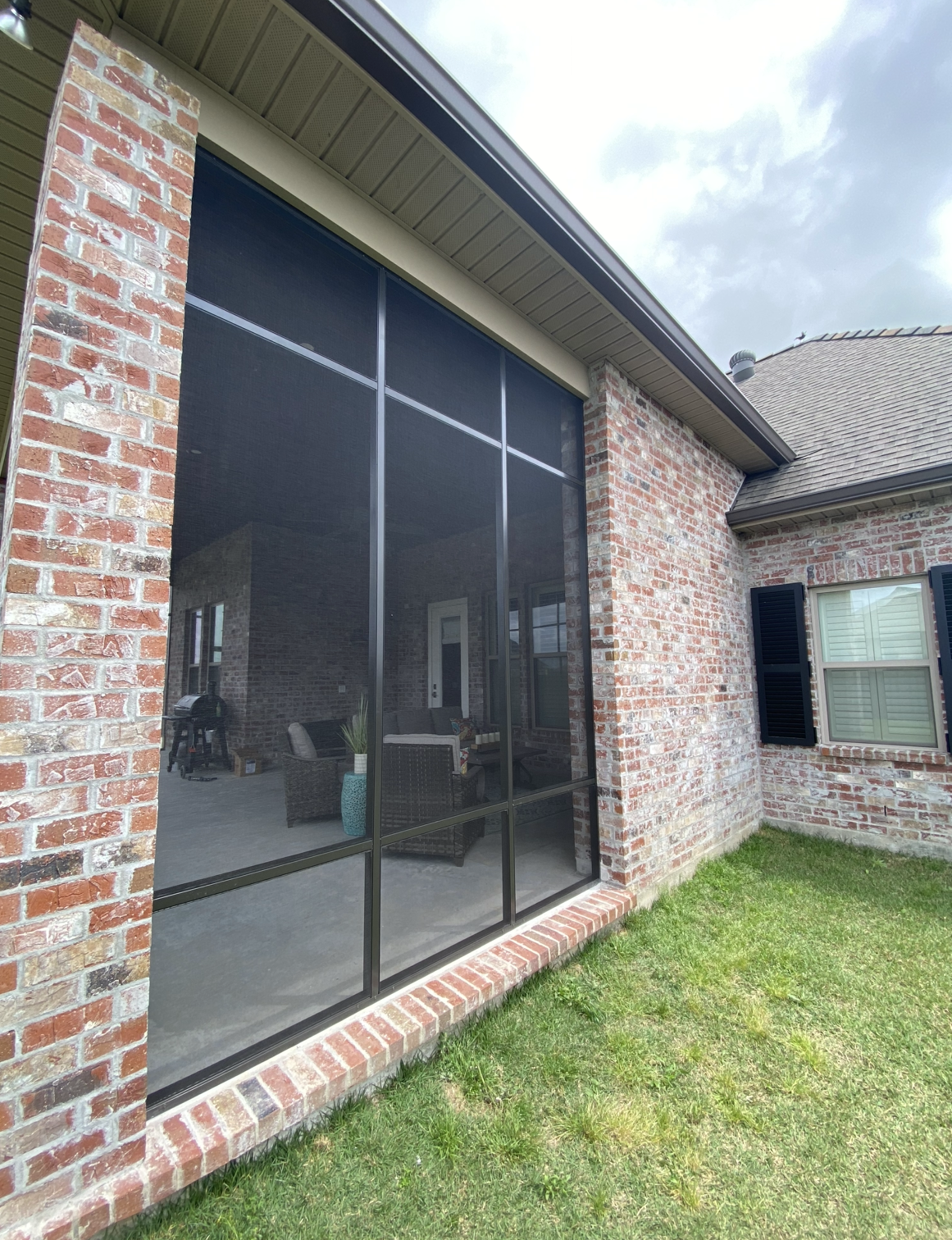 A brick house with a screened in porch and a large window.