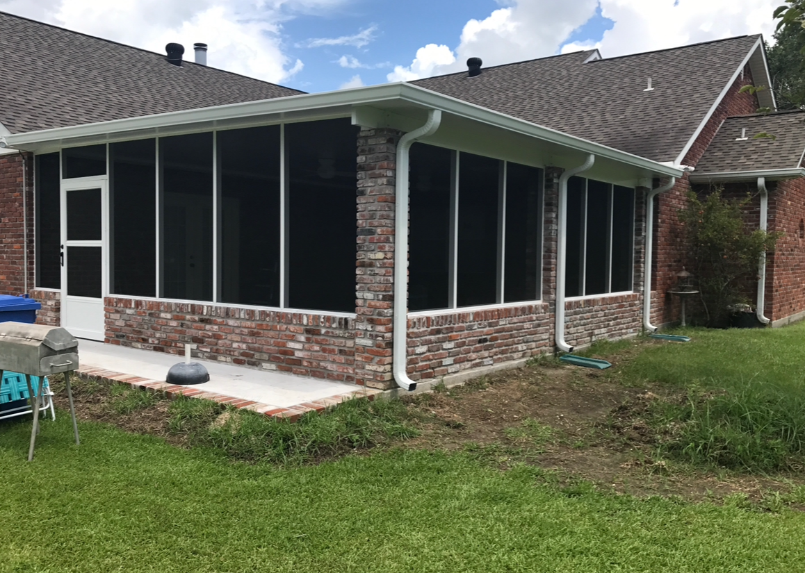 A screened in porch on the side of a brick house.