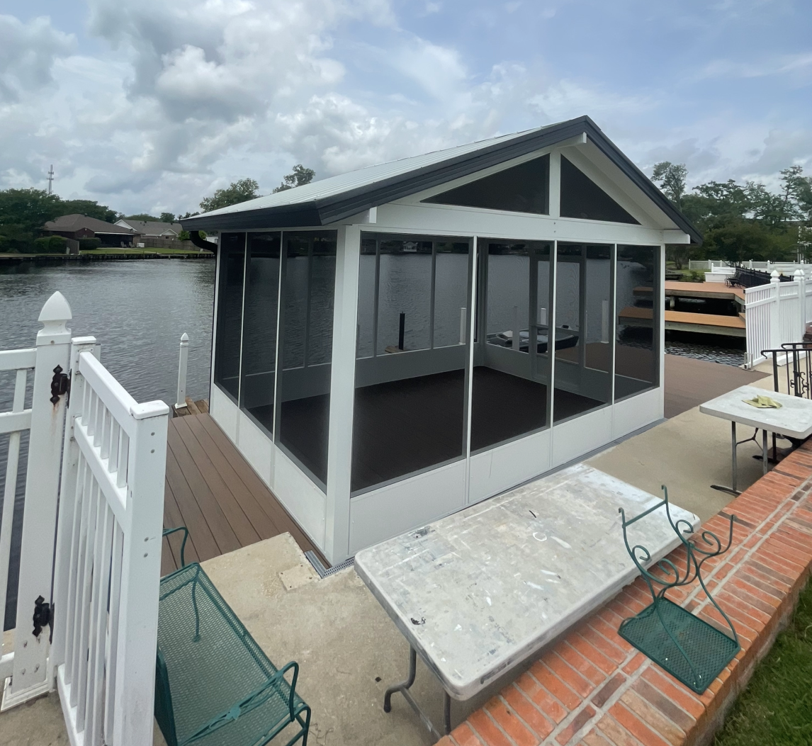 A screened in porch with a table and chairs next to a body of water.