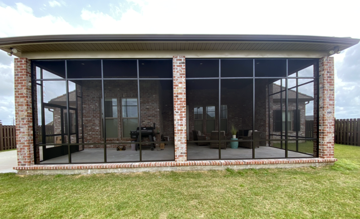 A screened in porch with a lot of windows and a brick house in the background.