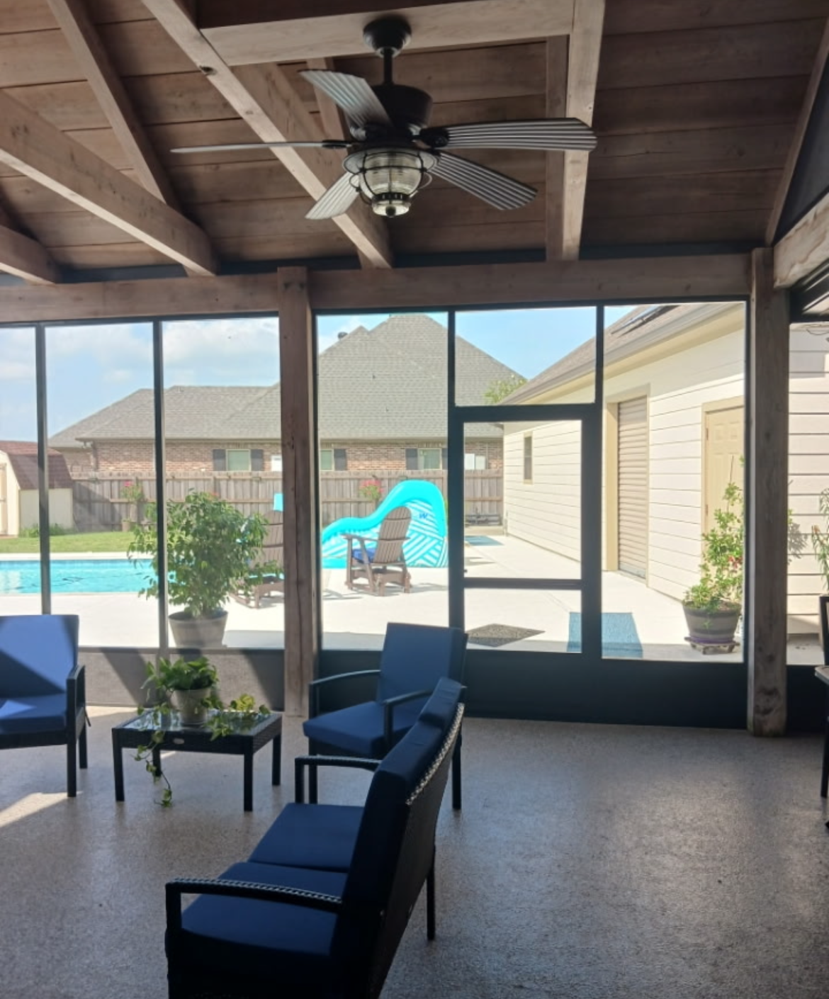 A screened in porch with chairs and a ceiling fan.