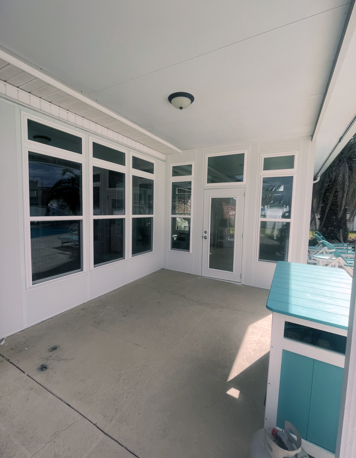 A large porch with lots of windows and a blue table.