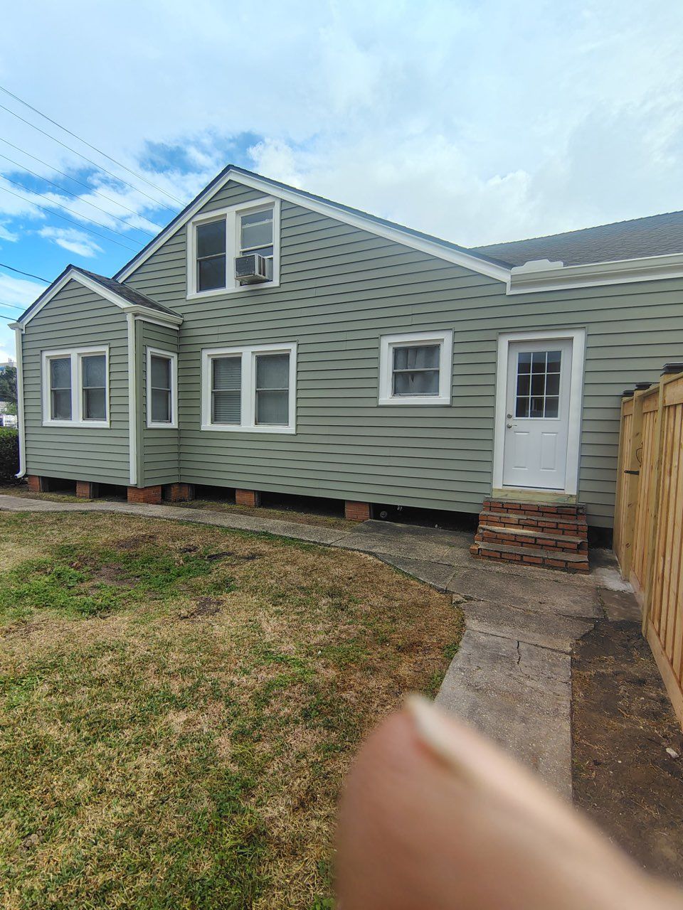 A side view of a light-green, single-story house with a white door, windows, and a paved walkway in a grassy yard.