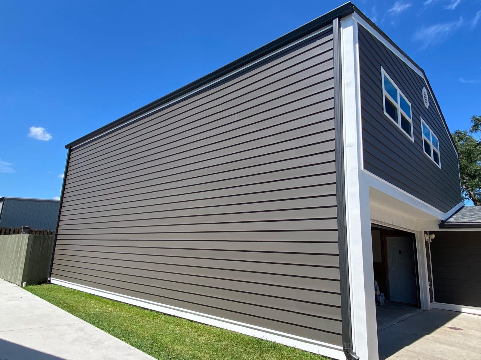 A two-story garage with dark brown horizontal siding, white corner trim, and two upper-level windows under a blue sky.