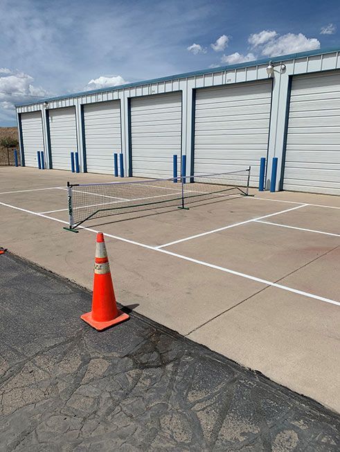 A tennis net is sitting in a parking lot next to an orange cone.