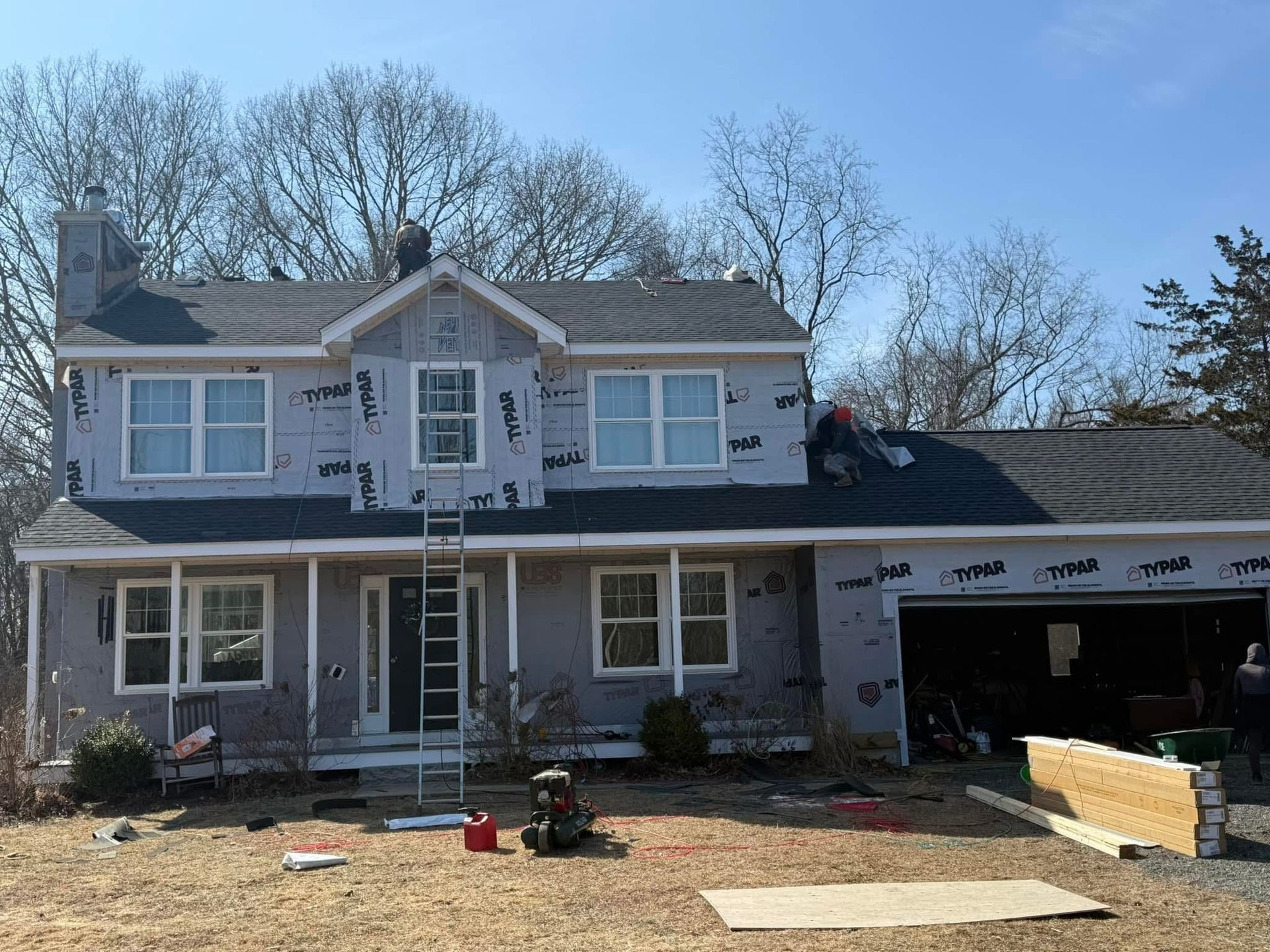 Two-story house under construction with new roof. Workers on roof, wrap around walls.