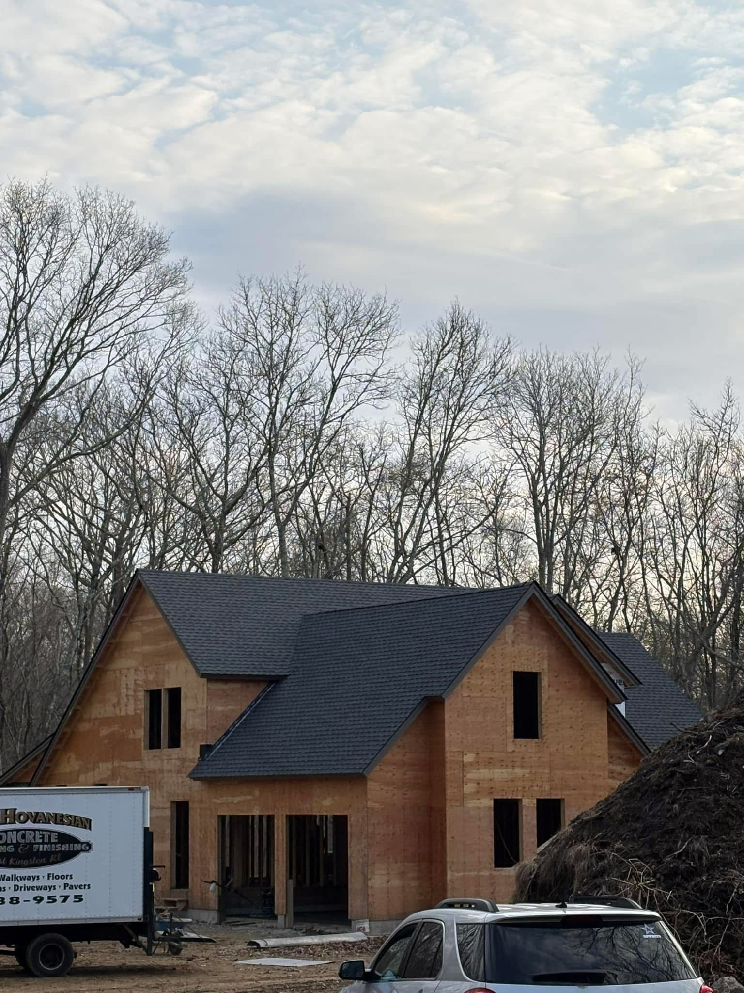 House under construction; wooden frame with black roof; parked truck and trailer.