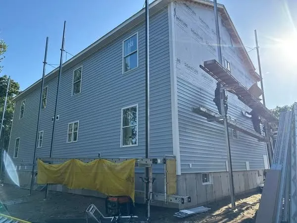 Two-story house under construction, light blue siding, scaffolding, workers on the side, sunny day.