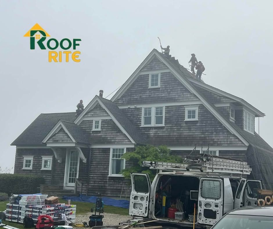 Workers repairing a gray shingled house roof beside a service van 