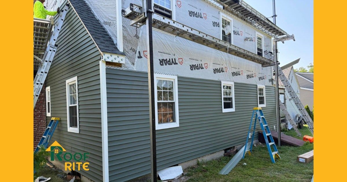 House exterior under renovation with new green siding. Wraps visible, ladders present.