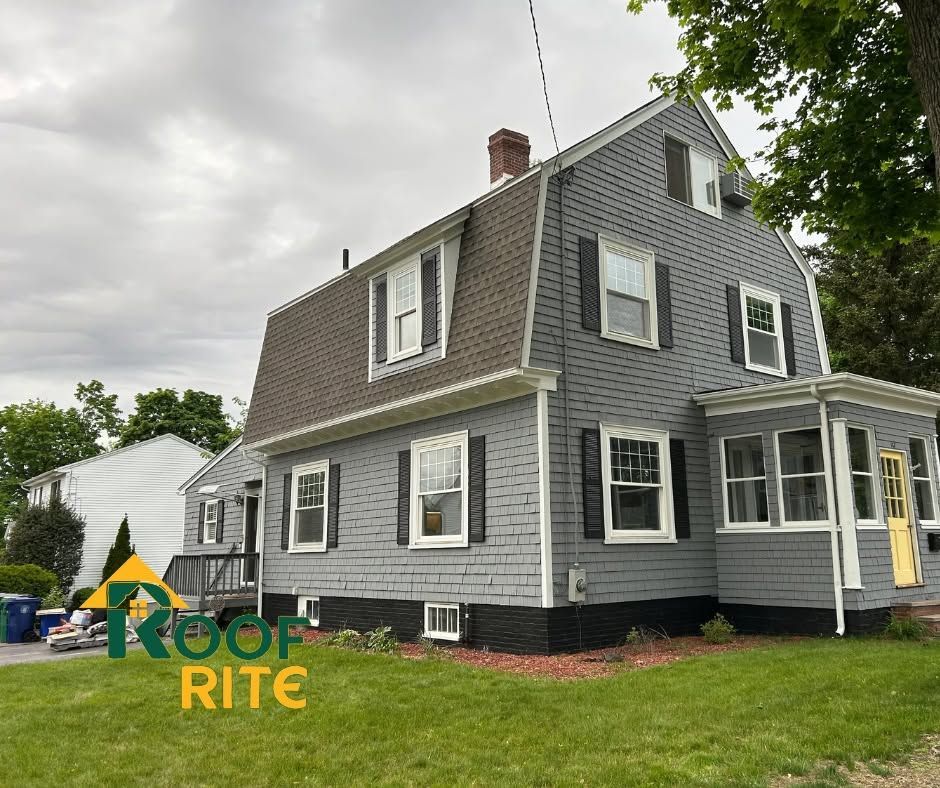 Gray two-story house with white trim and black shutters on a grassy lot under cloudy skies