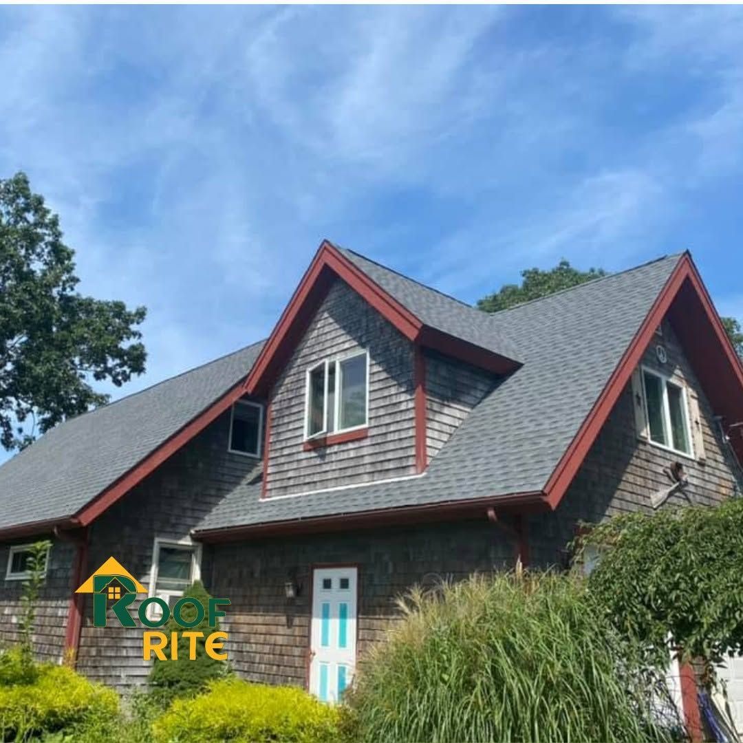 Two-story stone house with steep gray roof, red trim, and blue front door under a blue sky