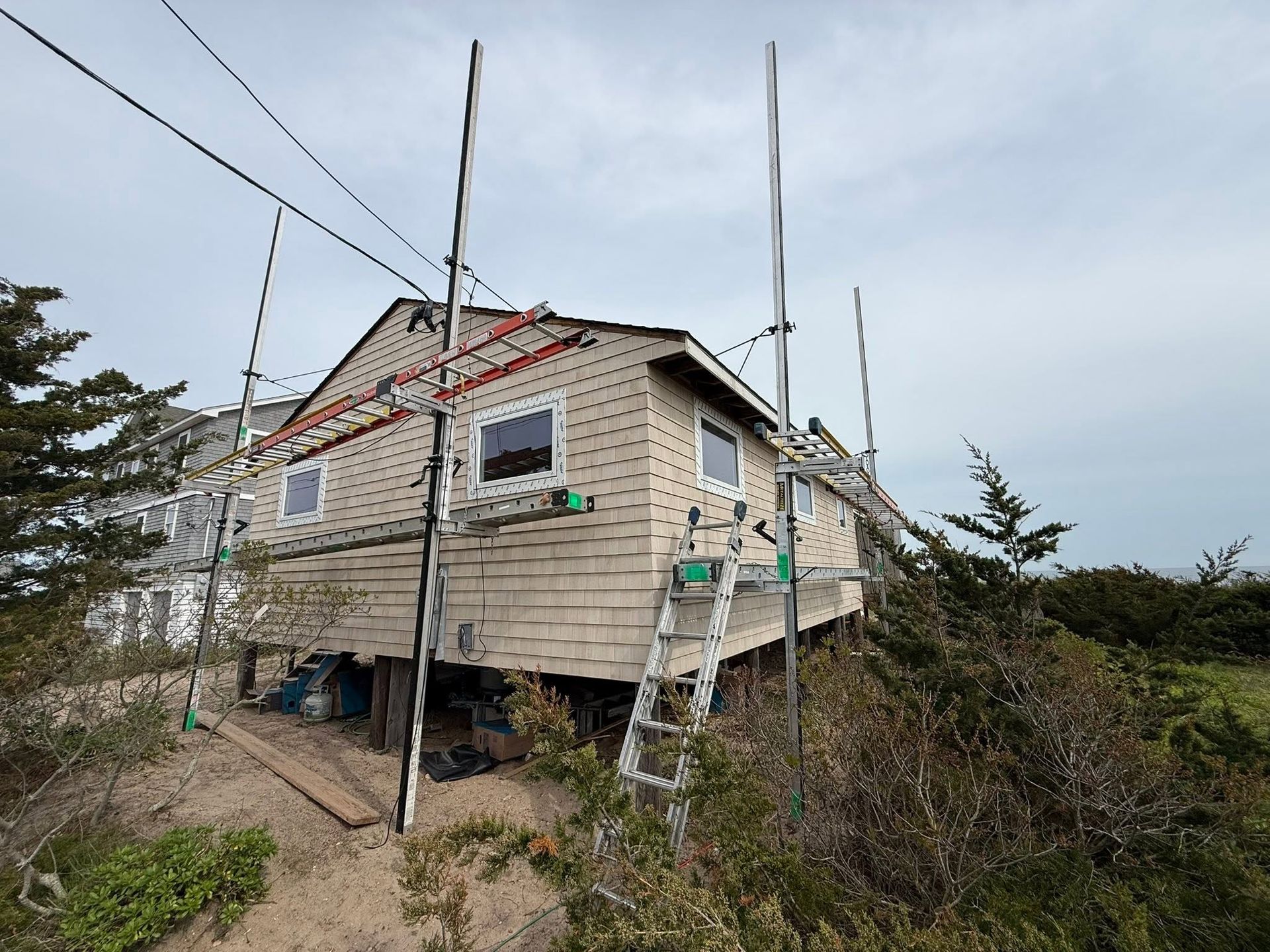 Small weathered house on stilts on a rocky hillside with utility wires and cloudy sky.