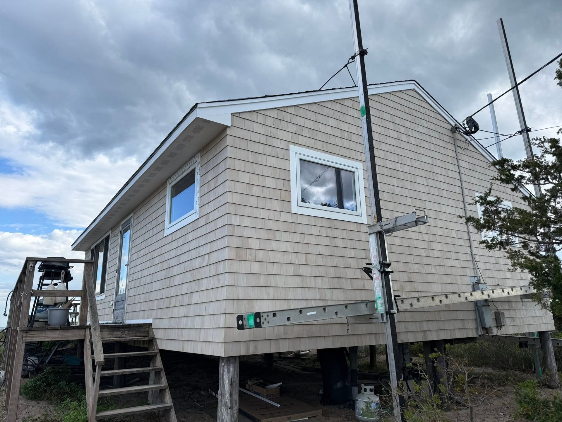 Small beige house on raised stilts with exterior stairs and antennas under a cloudy sky