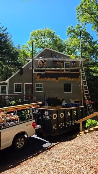 Workers on a house roof with ladders and a truck in the driveway on a sunny day