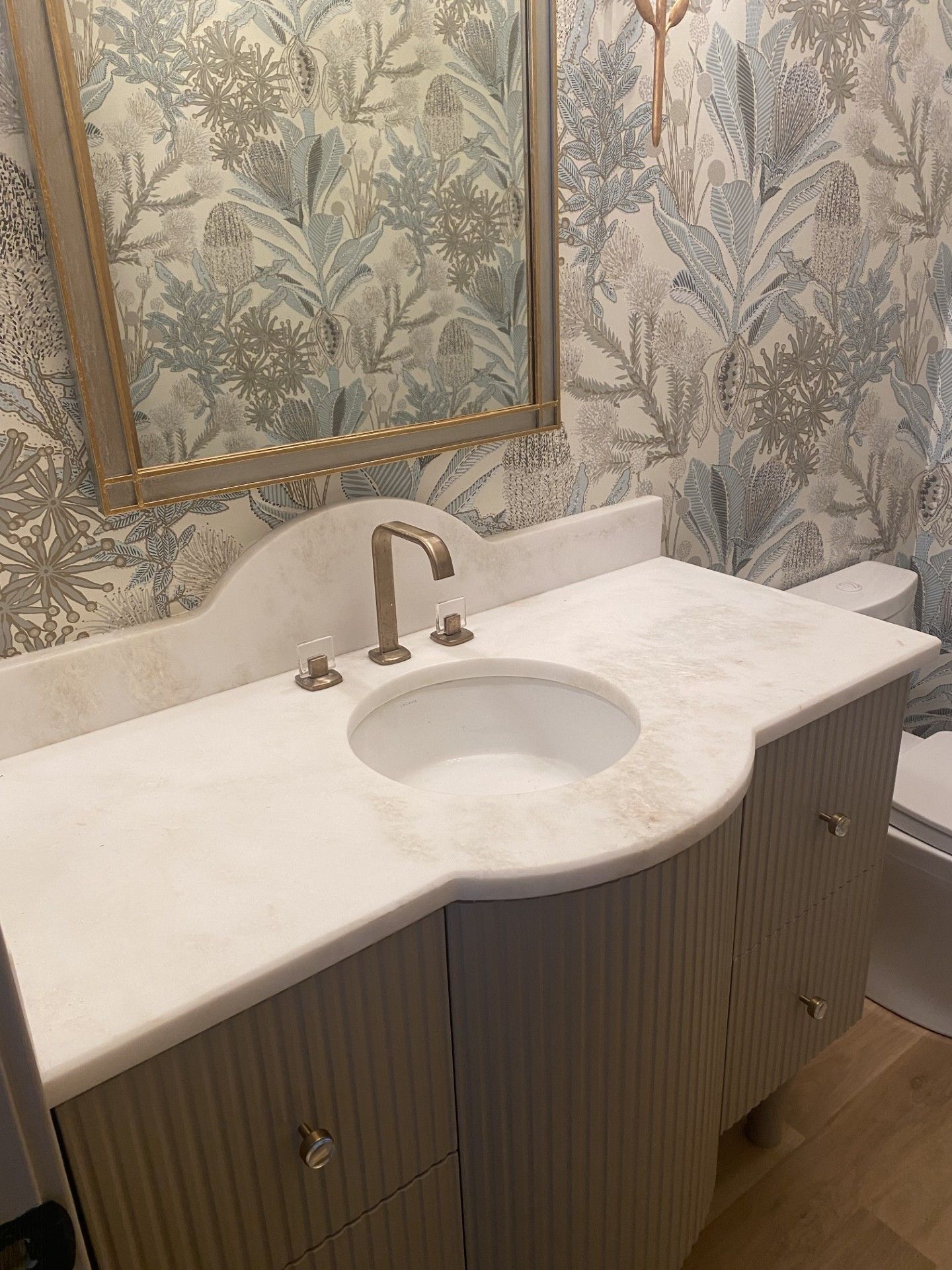 A bathroom with a sink , mirror and wallpaper.