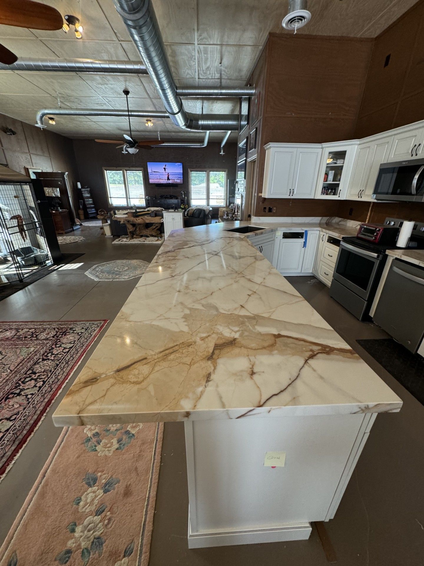 A kitchen with a long marble counter top and stainless steel appliances.