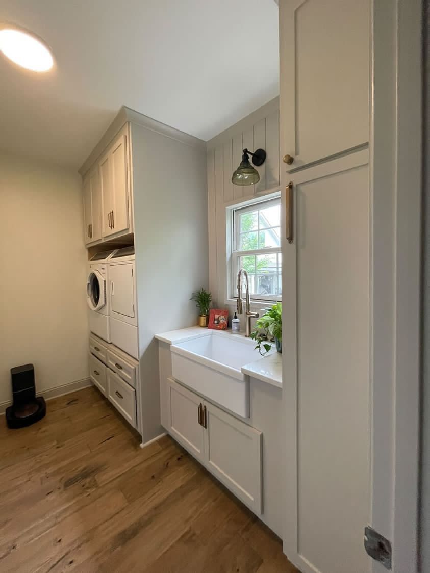 A laundry room with a sink , washer and dryer , and wooden floors.