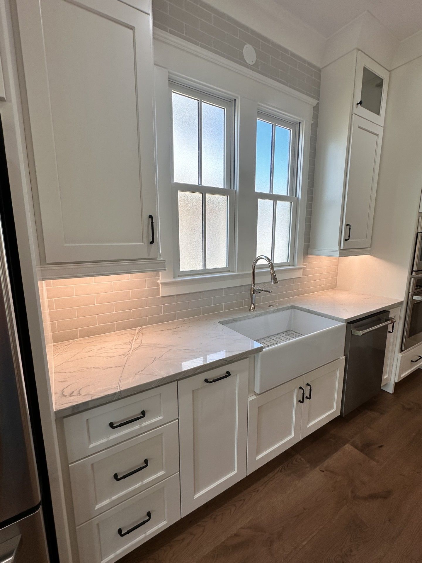 A kitchen with white cabinets , stainless steel appliances , a sink and a window.