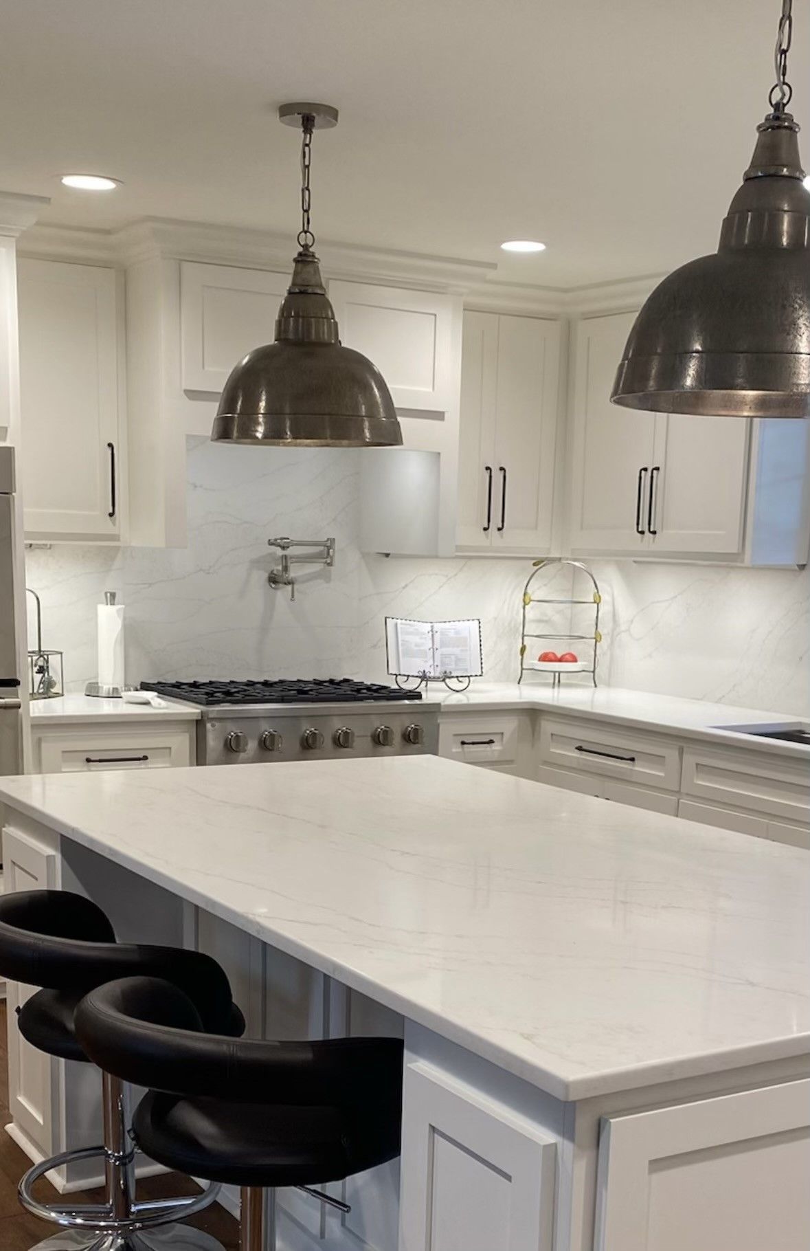 A kitchen with white cabinets , a large island , stools and a stove.
