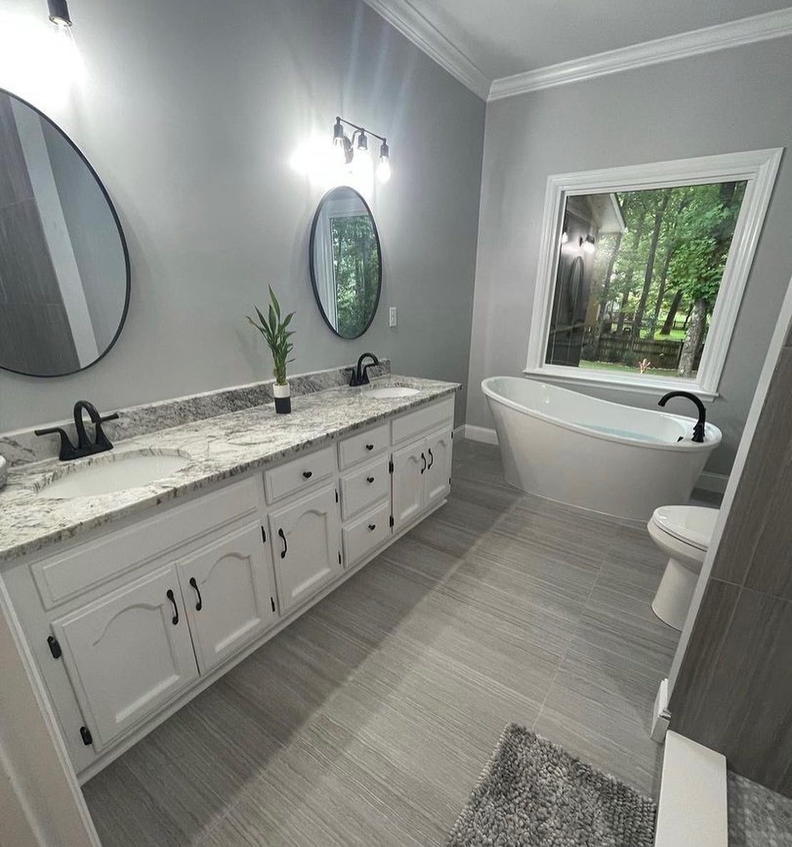 A bathroom with two sinks , a tub , two mirrors and a window.