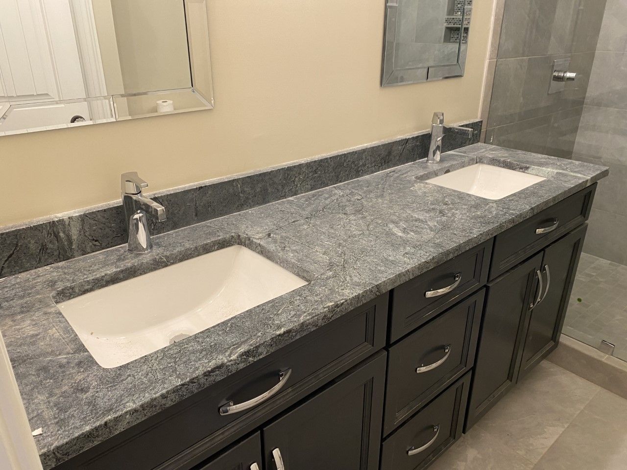 A bathroom with two sinks , a mirror and a walk in shower.