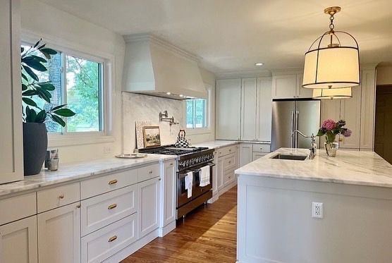 A kitchen with white cabinets , stainless steel appliances , marble counter tops and a large island.