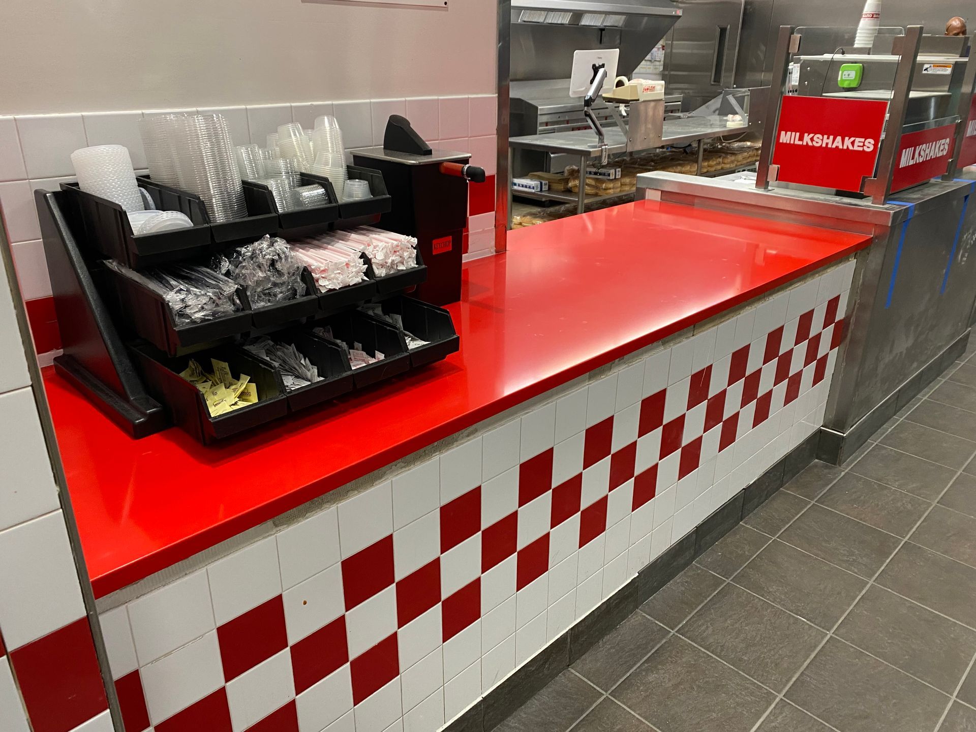 A fast food restaurant with a red counter top and checkered tiles.