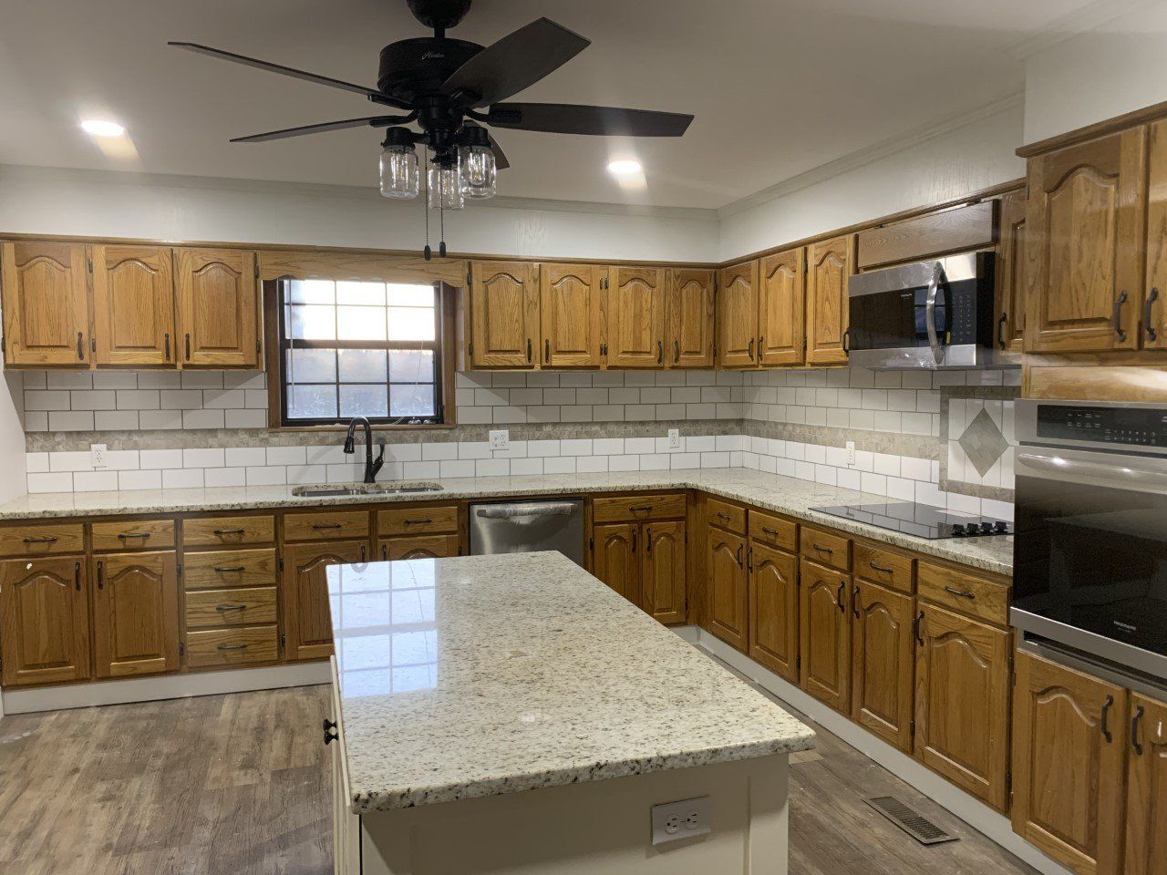 A kitchen with wooden cabinets , granite counter tops , stainless steel appliances and a ceiling fan.