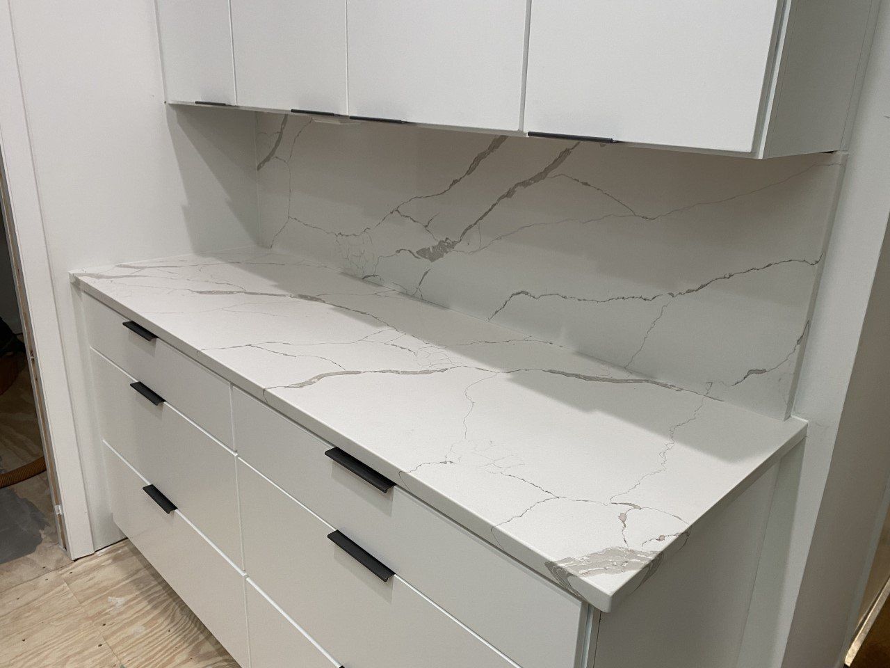 A kitchen with white cabinets and marble counter tops.