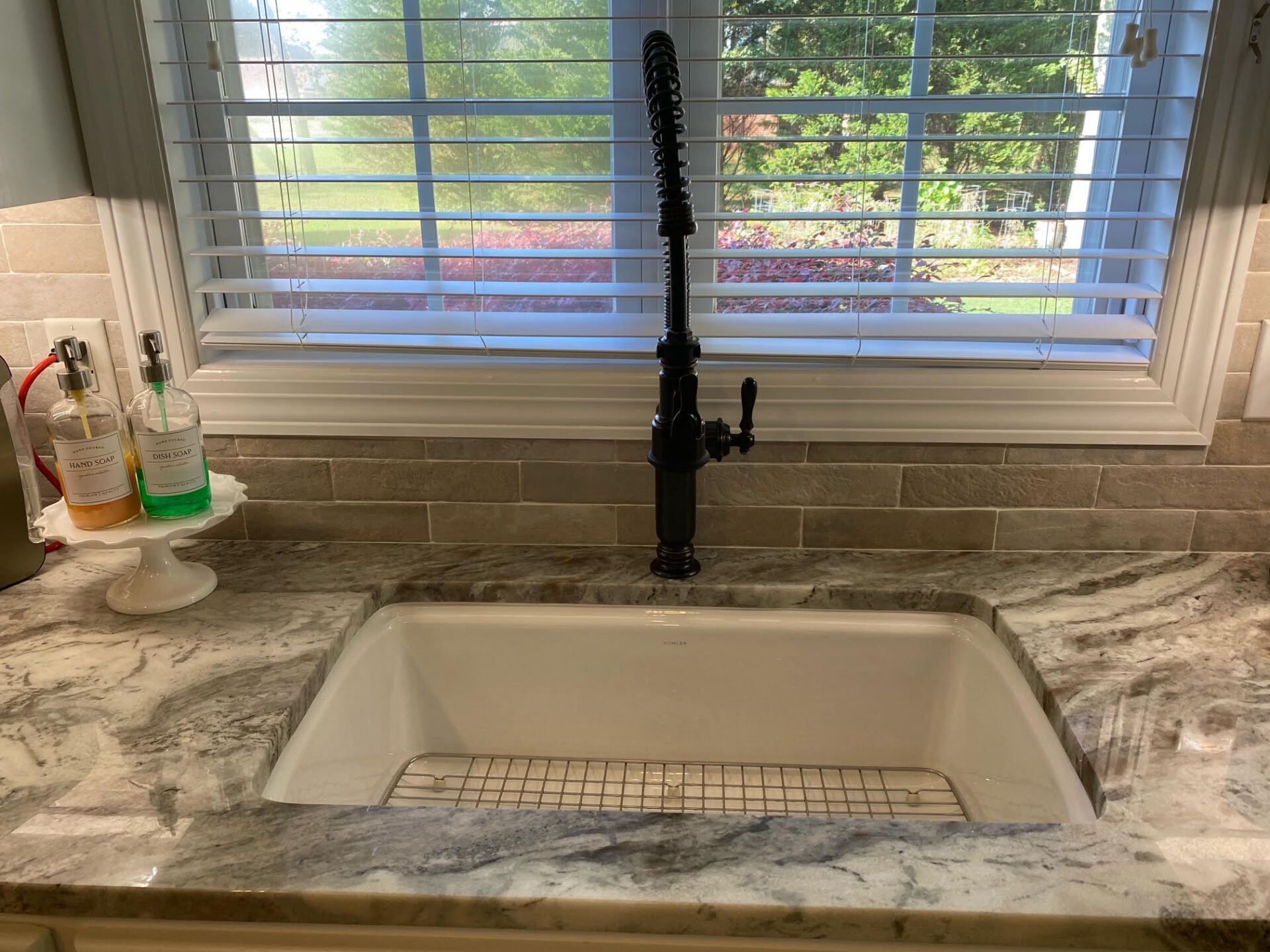 A kitchen sink with a black faucet and a window with blinds.