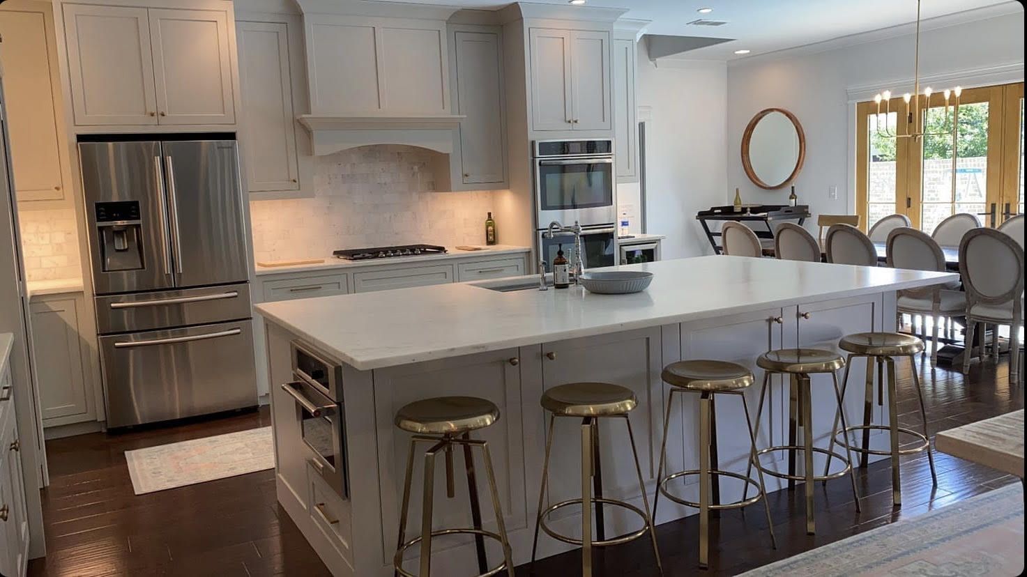 A kitchen with white cabinets , stainless steel appliances , a large island , and gold stools.