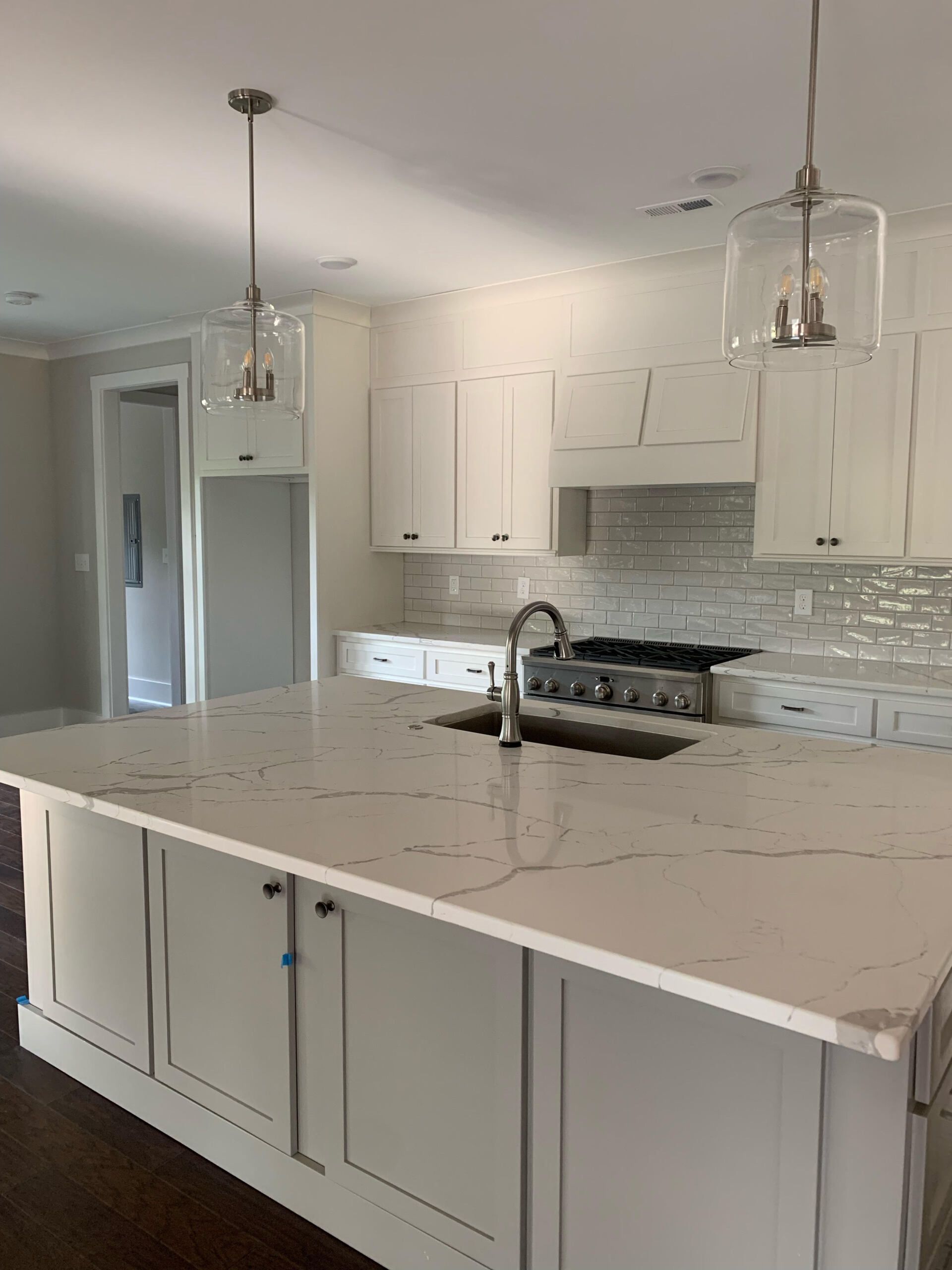 A kitchen with white cabinets , a sink , a stove , and a large island.