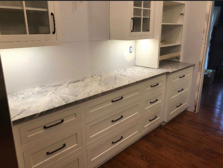 A kitchen with white cabinets and marble counter tops