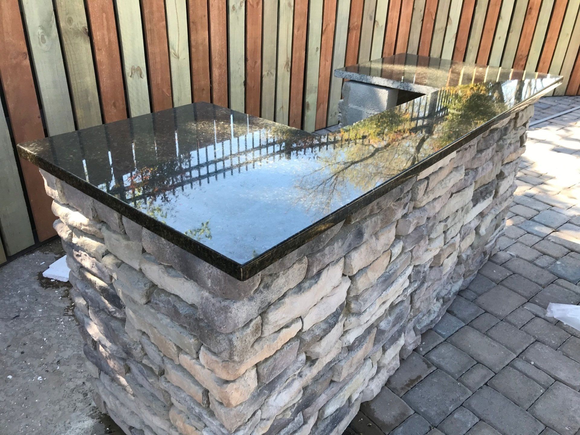 A stone bar with a black granite top is sitting on a brick patio.