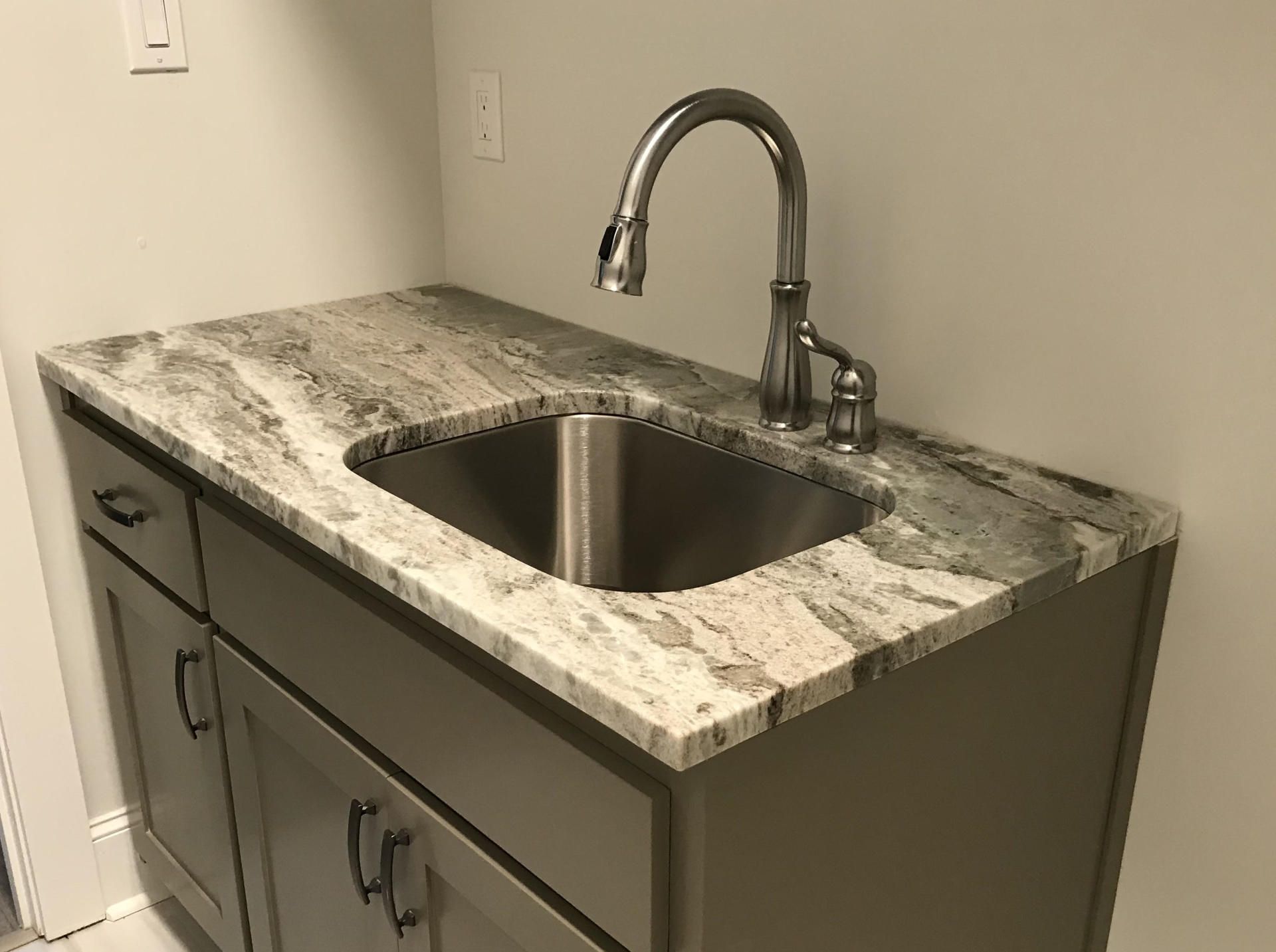 A kitchen sink with a faucet on top of a granite counter top.