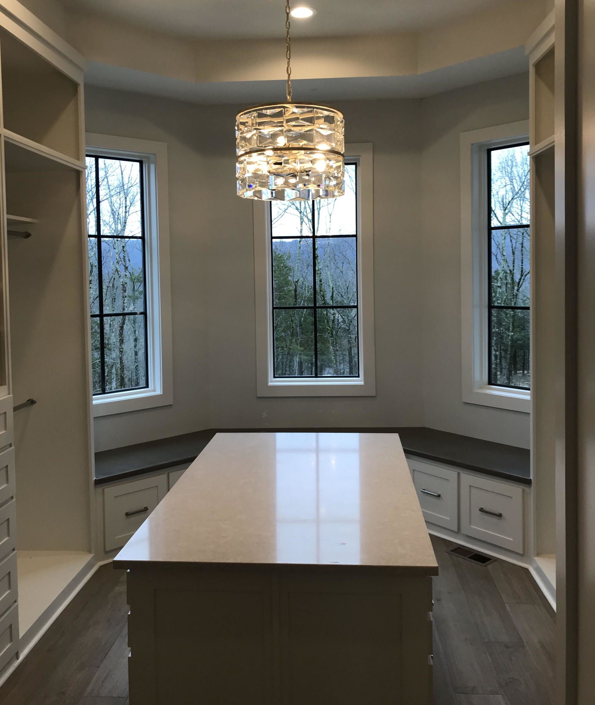 A walk in closet with a large table and a chandelier hanging from the ceiling.