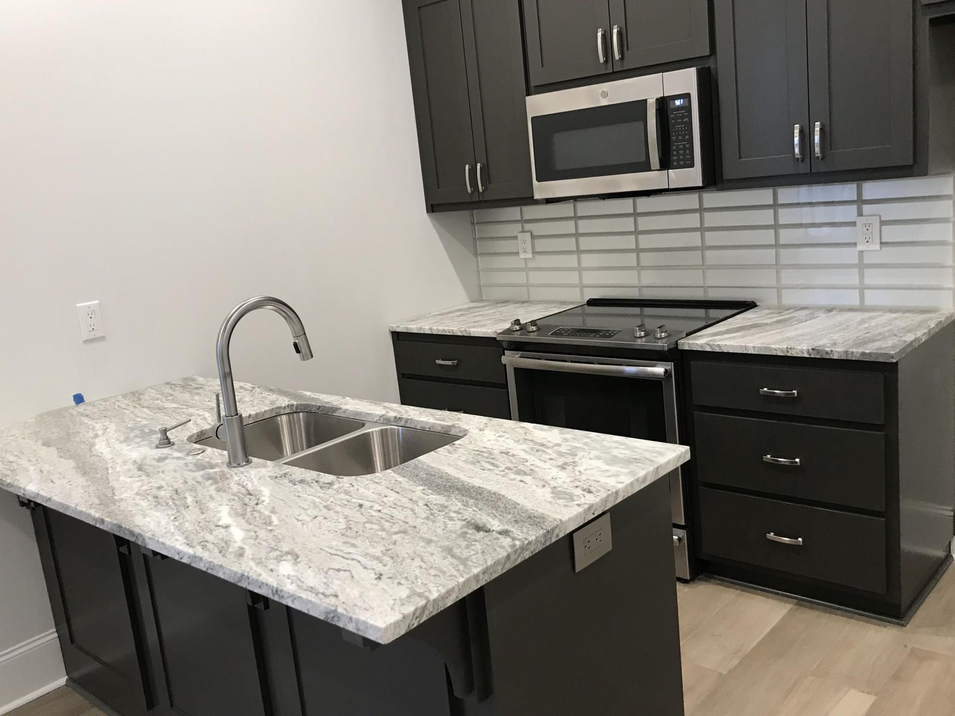A kitchen with a sink , stove , microwave and cabinets.