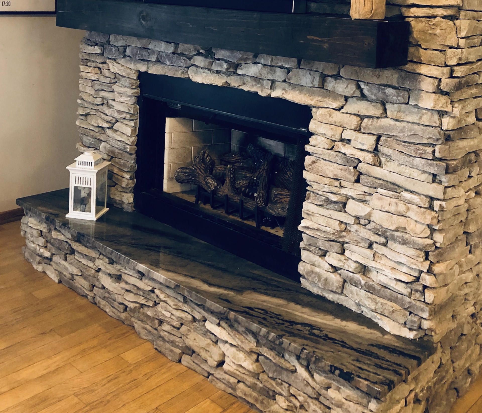 A stone fireplace in a living room with a lantern on the mantle.