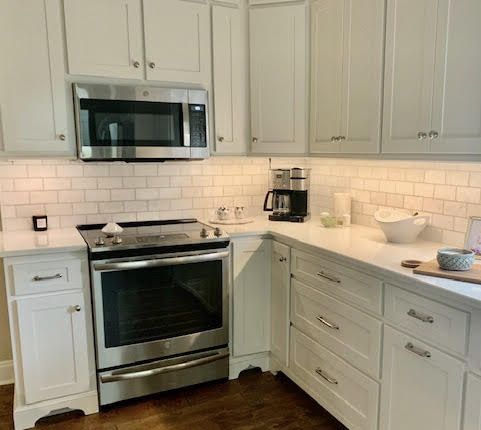 A kitchen with white cabinets , a stove , a microwave , and a coffee maker.