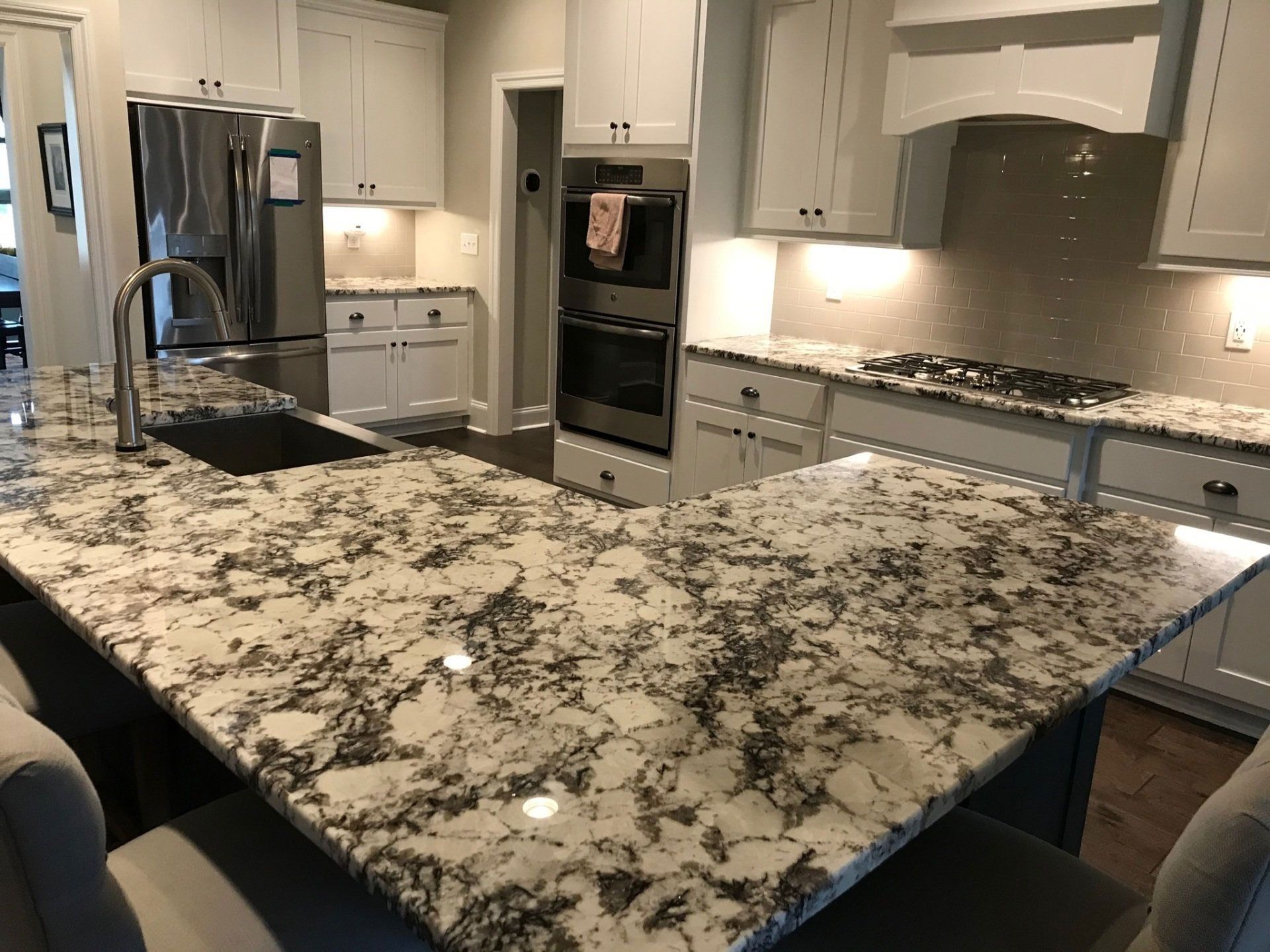 A kitchen with granite counter tops , stainless steel appliances , and white cabinets.