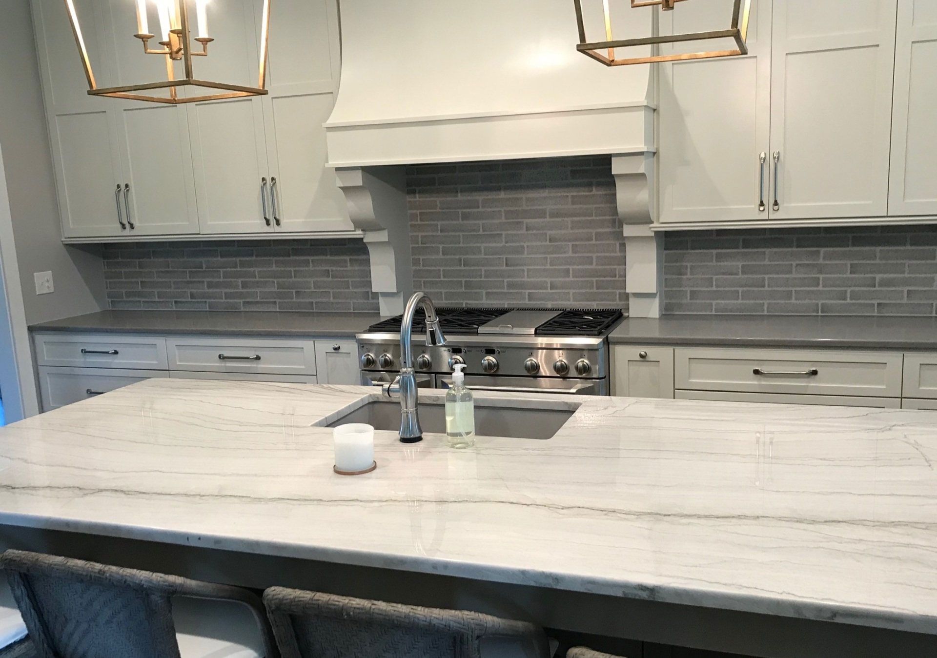 A kitchen with white cabinets , a stove , a sink , and a large island.