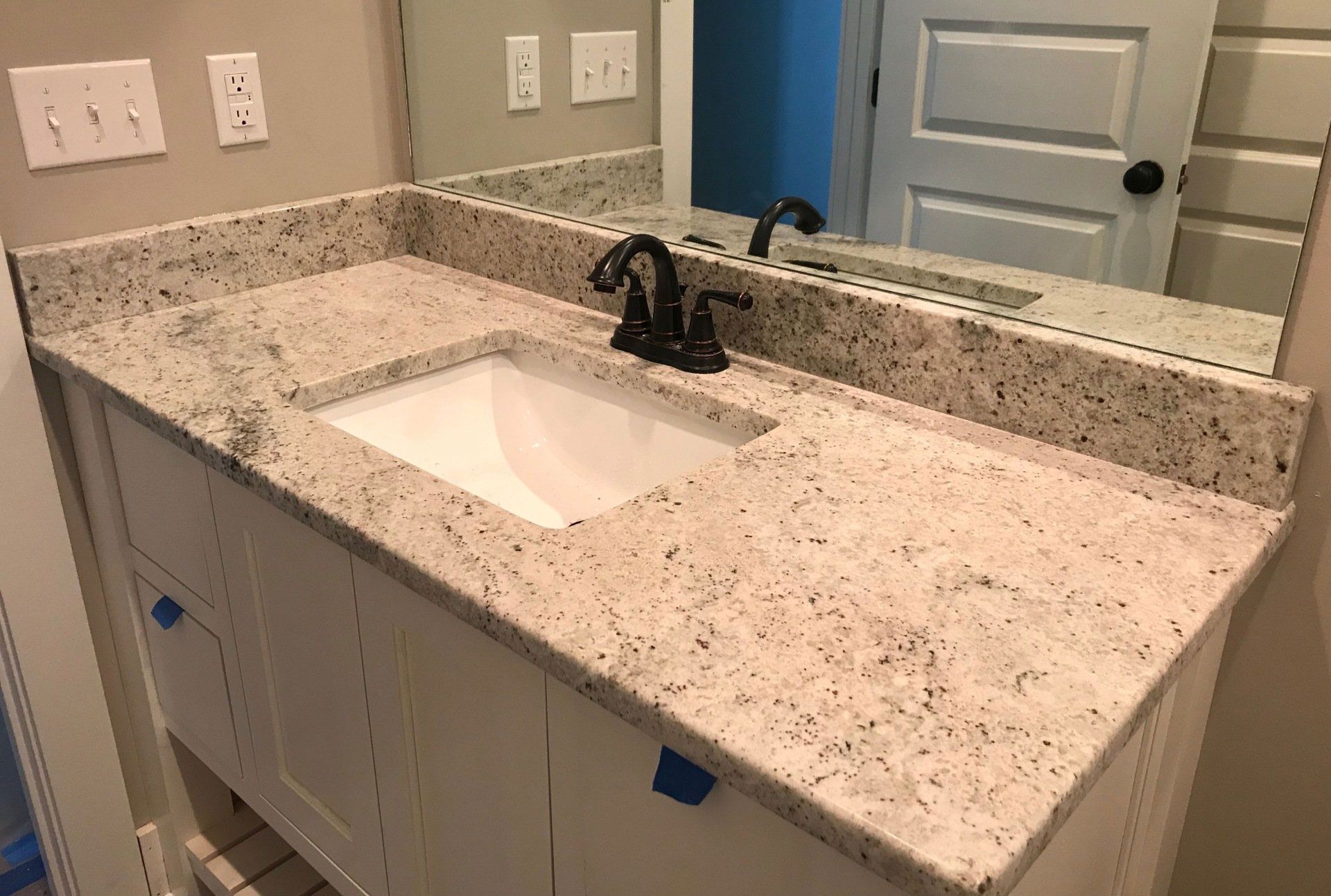 A bathroom sink with a granite counter top and a mirror.
